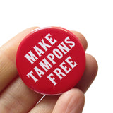 A round red 1.25" pinback button that reads MAKE TAMPONS FREE in a white fonts. Button is on a Social Alert Button backing card.