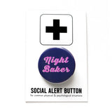 A round navy blue pinback button that reads NIGHT BAKER in a chunky pink script font, with a white drop shadow. Button is on Social Alert Button backing card.