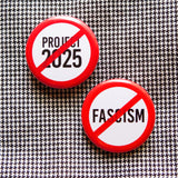 Two round white buttons, one reads NO PROJECT 2025 in black text with a red circle and slash to indicate being against Pro 2025. The other reads NO FASCISM with a red line & circle indicating being AGAINST FASCISM.