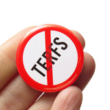 A round white button that reads NO TERFS in black text with a red circle and slash to indicate being against TERFS or against Trans Exclusionary Radical Feminists aka anti-trans feminists. Badge is held in a white hand.