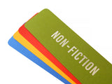 Four bright colored bookmarks fanned out, the top one is a moss green bookmark that reads NON-FICTION in silver embossed text. And there is an orange-red, marigold yellow and blue bookmarks fanned below, with no visible text.