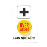 Round yellow pinback button that reads OVER WORKED in two lines of red text. Badge is on a Social Alert Button backing card.
