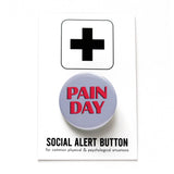 Round gray pinback button that reads PAIN DAY in a chunky red font with black drop shadow. Button is on a Social Alert Button Backing card.