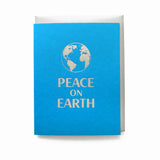 A bright blue A2 greeting card with a silver letterpress imprint of a planet earth illustration that reads PEACE ON EARTH. Card is paired with a silver envelope.