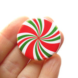 A red, green & white pinwheel pinback button that looks like a peppermint candy, held in a hand.