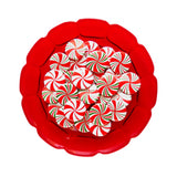 A bunch of round red, white & green pinback buttons that look like holiday peppermint candies. They on a vintage red glass plate.
