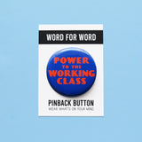 A round bold blue pinback button that reads POWER TO THE WORKING CLASS in red-orange text,  an art deco font. Button is on a Word For Word branded backing card that reads Pinback Button, Wear What's On Your Mind