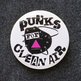 Round white 2.25" pinback button that reads Punks For Clean Air in a rough black font over the image of a studded black KN95 mask with a pink triangle.  Pinned to black denim.