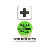 Round green pinback button that reads RAISE THE MINIMUM WAGE in black text. Button is on a Social Alert Button backing card.