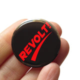 round black 1.25" pinback button that reads REVOLT! in thick red type. Button is held in a hand.
