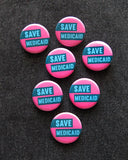 A bunch of round pink pinback buttons with light aqua text and dark teal boxes that reads SAVE MEDICAID. The 7 buttons are pinned to black denim.