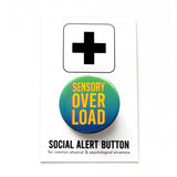 A round green to blue ombre 1.25" pinback button that reads SENSORY OVERLOAD in bright yellow text with a pink drop shadow. Button is on a Social Alert Button backing card.