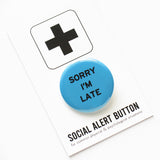Round medium blue pinback button that reads SORRY I'M LATE in black text. Pinned to a Social Alert Button backing card.