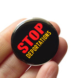 Round black pinback button that reads: STOP DEPORTATIONS in red and yellow text. Button is held in a hand.