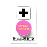 Round vibrant pink pinback button reading SWEET TOOTH in yellow text. Pinned to a Social Alert Button backing card.
