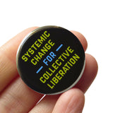 A round black pinback button with lime green and blue  text that reads SYSTEMIC HANGE FOR COLLECTIVE LIBERATION. The Button is held in a hand.
