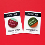 Two round pinback buttons: left is wine red, pink & mint green and reads TIPSY AUNT. Right button is dark green background, mint green text that reads DRUNK UNCLE and a little half moon of whisky orange-brown at the bottom, to look like a partially drunk cup of whiskey. These buttons are on a perforated backing card that tears down the middle. Each Half reds PERFECT PAIR, Pinback Button, left side reads KEEP ONE. Right side reads SHARE ONE.