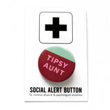 A round pinback button that looks like a tilted glass of wine. The bottom half is wine red burgundy with an angled top, mint green above. And inside the wine color it reads TIPSY AUNT in pink askew letters. Button is pinned to a Social Alert Button backing card.