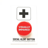a round red pinback button reads: VISUALLY IMPAIRED in light blue text. Button is on a white Social Alert Button backing card with a black plus sign at the top.