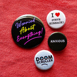 Four colorful pinback buttons on a red denim background. Three 1.25” buttons that reads I Heart Steve Kornacki, Anxious & Doom Scroller with one 2.25” black button that reads Worried About Everything in 3 neon colors.
