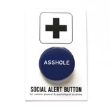 Round navy blue pinback button that reads ASSHOLE in white san serif text. Button is on a Social Alert Button backing card with a black plus sign at the top of the white card.