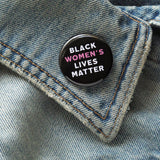 Round black pinback button that reads BLACK WOMEN'S LIVES MATTER, in white with Women's in pink for emphasis. Button is on a denim lapel.