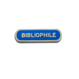 Long capsule shaped enamel pin that says BIBLIOPHILE.  Silver text and outline on a royal blue enamel background.