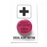 dark raspberry color pinback button that reads Bodily Autonomy Is A Human Right in dark red. Button is on a Social Alert Backing Card