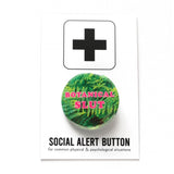 Round pinback button that says BOTANICAL SLUT. Pink text on a fern photo background. Pinned to a Social Alert Button backing card.