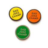 Round enamel pin the says DAD JOKE CHAMP.  In three different color choices.  Gunmetal text and outline with a yellow enamel background. Gunmetal text and outline with an orange enamel background. And silver text and outline on a green enamel background.