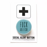 A round pale teal pinback button that reads FUCK ABLEISM in a dark teal color, in a condensed sans serif font.  The pinback button is on a white backing card with a thick plus sign at the top of the card. On the bottom it reads Social Alert Button, for common physical & psychological situations.
