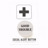 A round off-white pinback button that reads GOOD TROUBLE in black text. Button is on a Social alert Button backing card