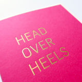 Magenta greeting card that says HEAD OVER HEELS.  Close up of the gold hot foil pressed text.