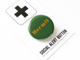 Shiny round dark green button with goldenrod serif text that reads: HERMIT. Hermit button is on a black & white branded card with a large plus sign at the top, and reads Social Alert Button at the bottom of the card, beneath the button