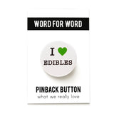 Round white button that reads I LOVE EDIBLES. Love is indicated with a green heart symbol, the remaining text is black. Button is on a Word For Word branded backing card.