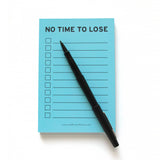 Light blue 4x6" inch notepad. Reads NO TIME TO LOSE at the top in a black sans serif font. Eleven check boxes line the left side of the page, with lines to write your task on the write. Small text listing word for word factory's website www.wordforwordfactory.pro at the bottom. Uncapped Paper Mate black pen lies on the pad diagonal, ready to write a list