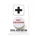 White round pinback button that reads NUTCRACKER in red san serif text.  Button is on a Social Alert Button backing card.