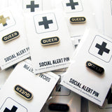Pile of queer enamel pins on Social Alert Pin backing cards.