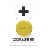 A round yellow 1.25" pinback button that rads SENSITIVE in thin black text. Badge is on a Social Alert Button backing card.
