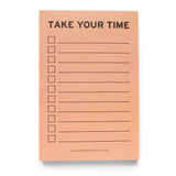 Vertical rectangle notepad with peach background, reading TAKE YOUR TIME in black text at the top, with left justified check boxes and lines to write on to the right. The brand's website is listed small at the bottom of the notepad: www.wordforwordfactory.pro