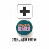Round teal colored pinback button which reads Voracious Reader in sans serif font. Voracious is in peach, Reader is a larger word and in lavender. The button is on a white Social Alert Button backing card with a black plus sign at the top.