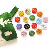 A bunch of shiny round multi-colored pinback buttons coming out of a green felt stocking: Buttons read -- Drunk Uncle, Egg Nog Fog, Star Baker, Sugar Plum Fairy, Lump of Coal, Naughty/Nice, Re-Gifter, Present Peeker, Jewish, Food Coma, Latke Lover, Gay Apparel, Nut Cracker, Fruit Cake, Candy Cane Licker and more