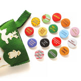 A bunch of shiny round multi-colored pinback buttons coming out of a green felt stocking: Buttons read -- Drunk Uncle, Egg Nog Fog, Star Baker, Sugar Plum Fairy, Lump of Coal, Naughty/Nice, Re-Gifter, Present Peeker, Jewish, Food Coma, Latke Lover, Gay Apparel, Nut Cracker, Fruit Cake, Candy Cane Licker and more 