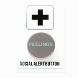 Product photo of a 1.25" pinback button on a cardboard social alert backing card.  The background of the button is gray and the light blue text says FEELINGS