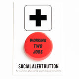 A round red-orange pinback button that reads WORKING TWO JOBS in black text. Button is on a Social Alert Button backing card.