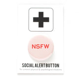 A round light pink pinback button with dark pink text that reads NSFW stands for Not Safe For Work. Button is on a Social Alert Button facing card.